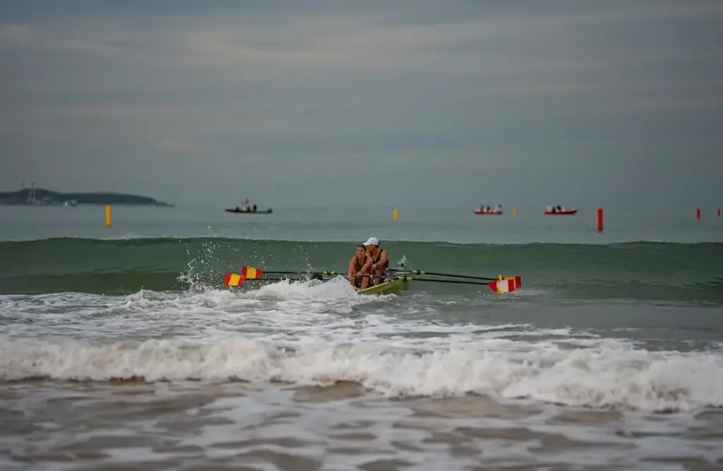 Doble mixto español con palas de los colores de España superando una ola en el Mundial de Beach Sprint de Qingdao