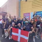 Integrantes del equipo de dragon boat del Club Náutico Santa Lucía posan con la bandera de Cartagena ante los carteles del VIII Jan Collins Memorial e Intercontinental Dragon Boat Festival en San Pedro del Pinatar